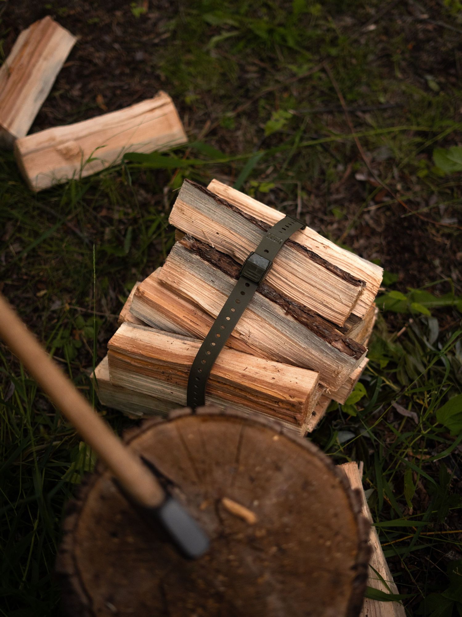 Bundled firewood pieces secured with dark straps on wooden stump outdoors.