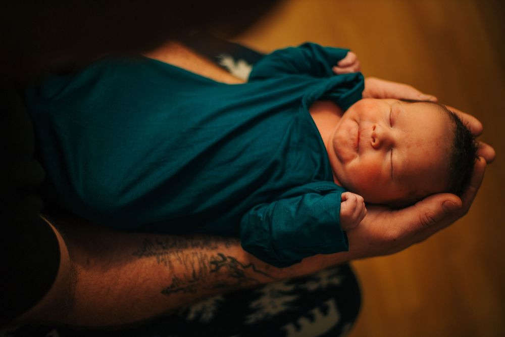 Newborn baby wrapped in teal swaddle blanket sleeping peacefully during professional photoshoot.