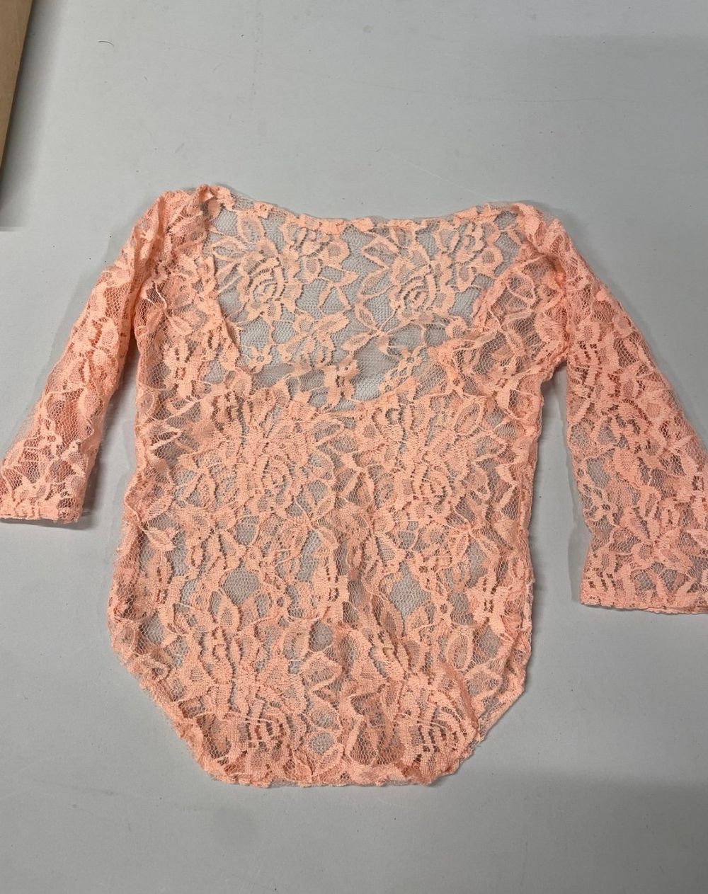 Peach-colored lace crop top with three-quarter sleeves laid flat on a gray surface.