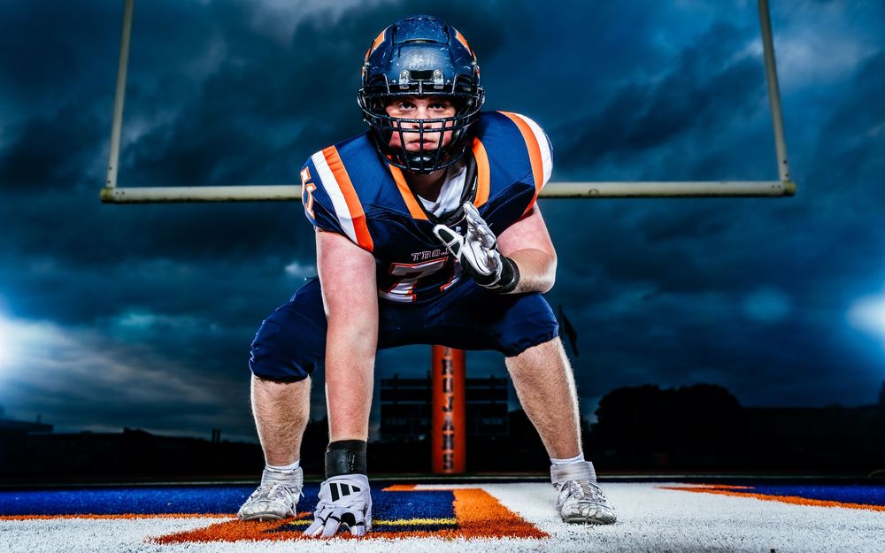 Hershey Trojans football lineman Media Day portrait in three-point stance with dramatic sky background, by Deanna Fox, SportsFox Photography