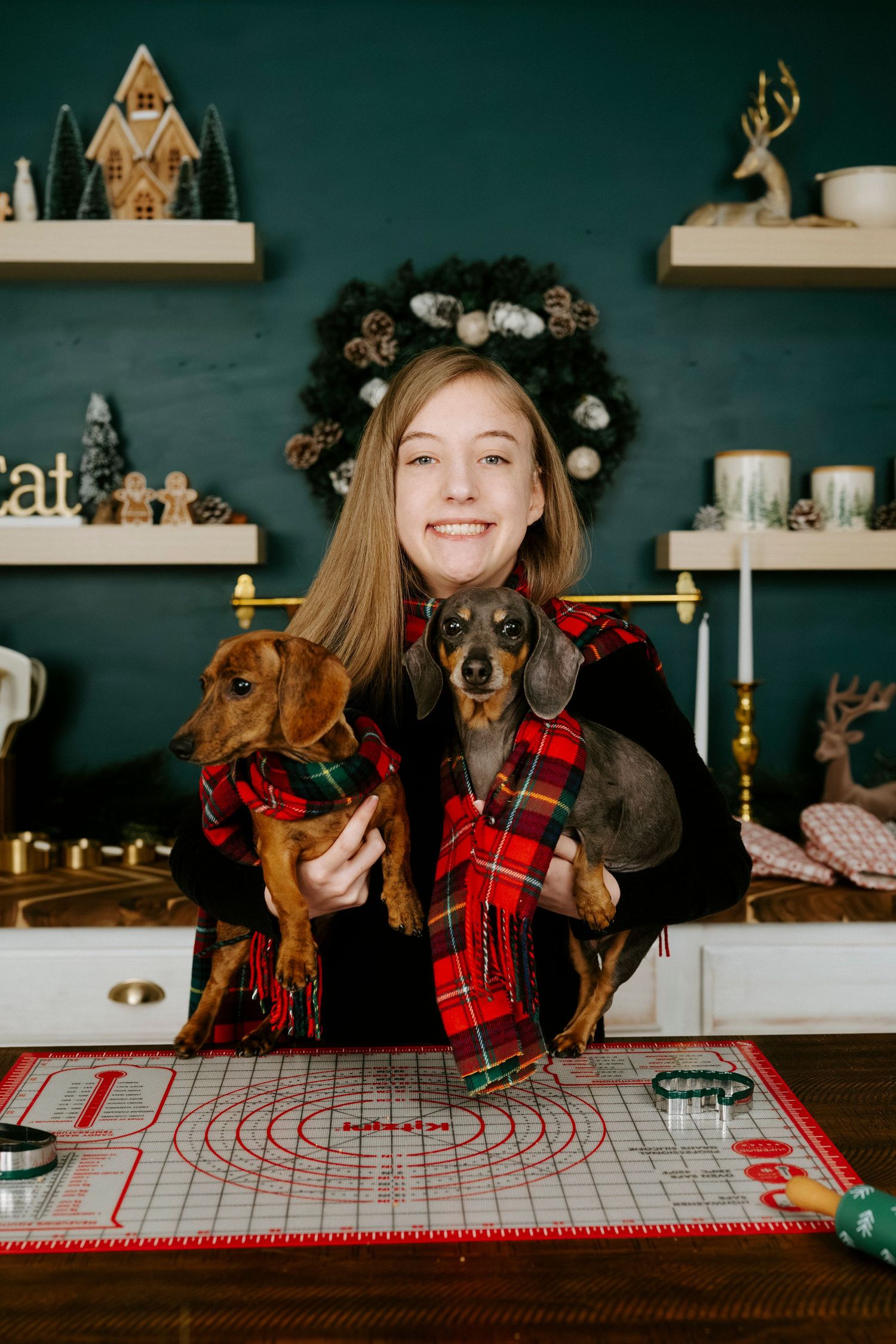 Dog and owner in plaid shirt pose playfully on wooden table with holiday decorations and checkered tablecloth.
