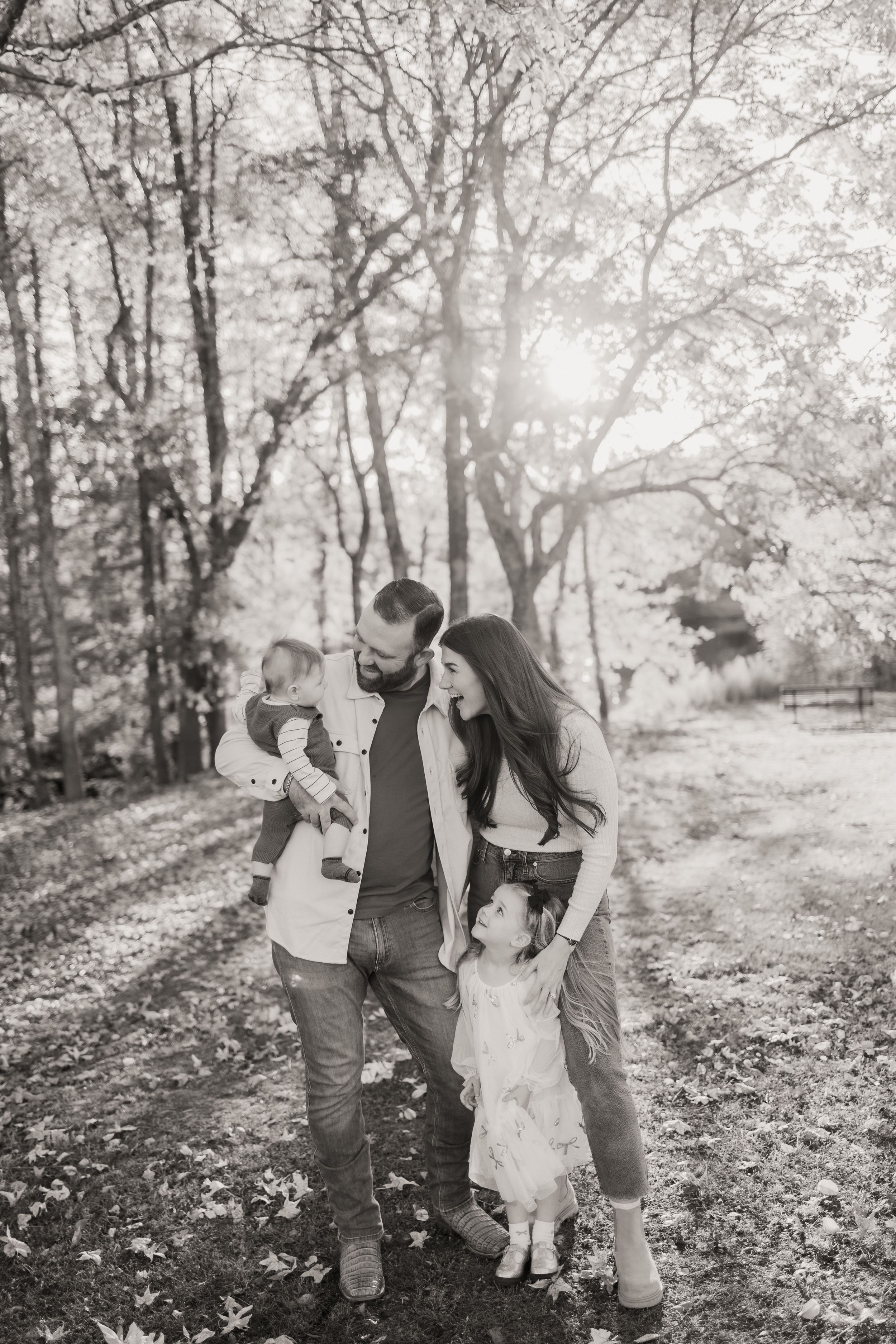 A family shares joyful moments together on a sunlit autumn day in a wooded park setting.