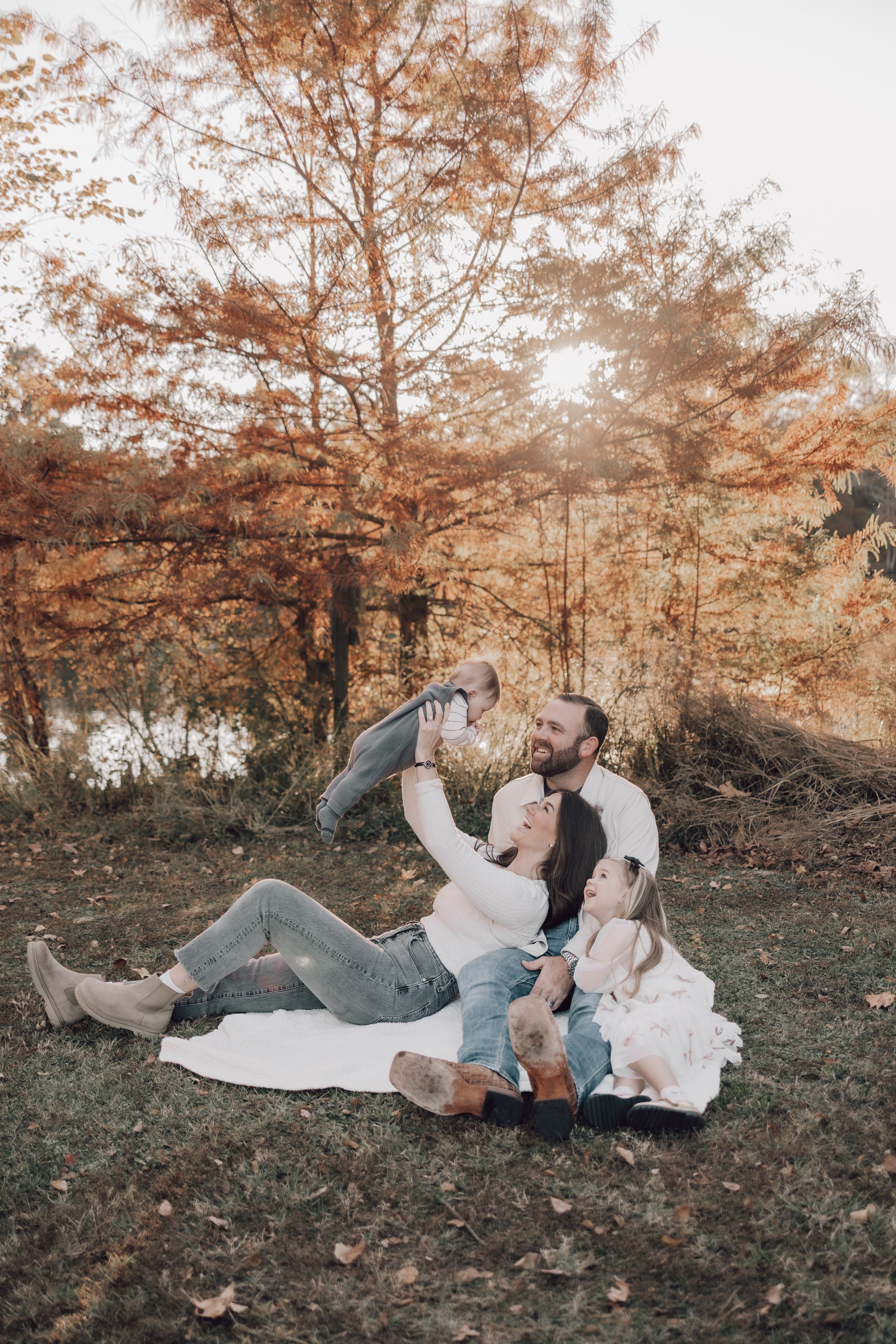 Family lying on a blanket together during an autumn photoshoot with warm orange tones in the background.