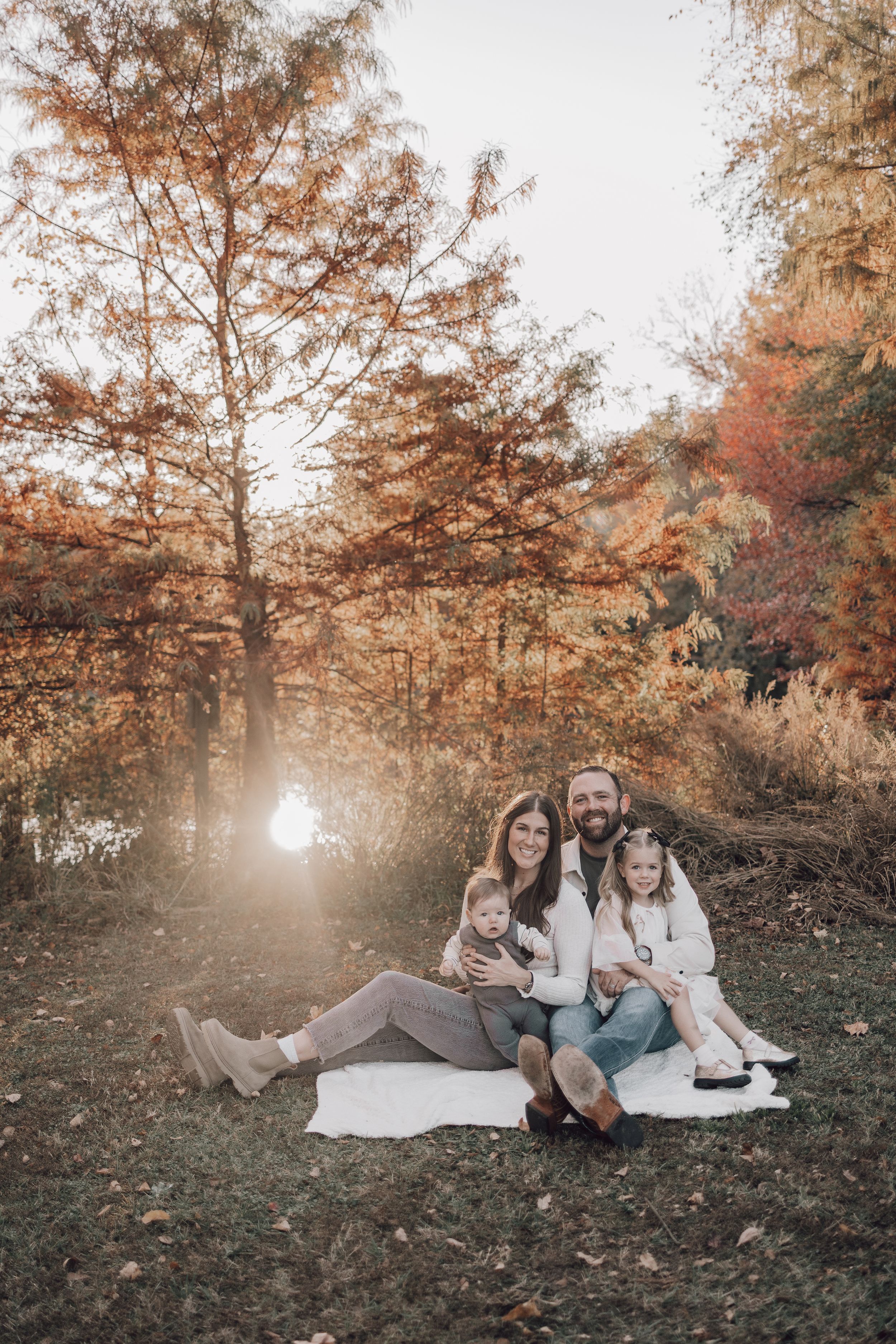 A family sits together on a blanket during an autumn photoshoot with golden sunlight filtering through fall foliage.