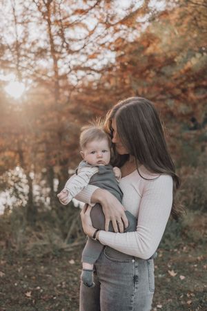 A tender outdoor autumn moment captured in warm tones as a baby is held close in a natural setting.