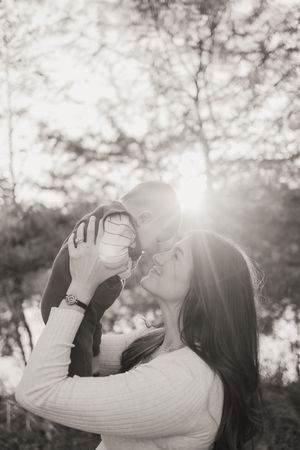 Two people share an intimate moment in white sweaters as sunlight creates a dreamy backlit glow through trees.