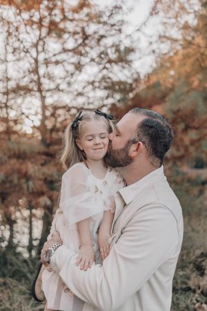 A parent and young child share tender moments outdoors during a fall photoshoot wearing coordinating white outfits.