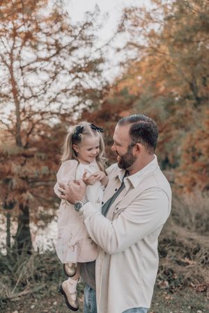 A tender autumn moment outdoors with warm neutral tones and fall foliage in the background.