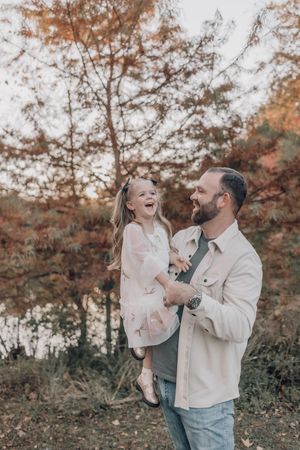 A joyful family moment captured outdoors during autumn with warm lighting and fall foliage in the background.