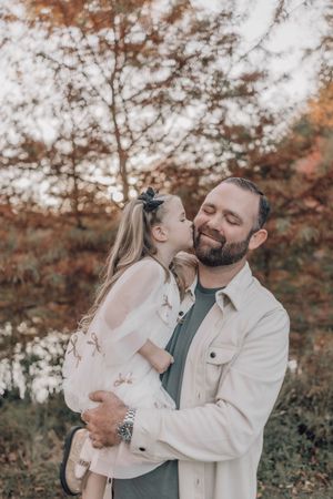 A tender family moment captured outdoors during autumn with warm fall colors in the background.