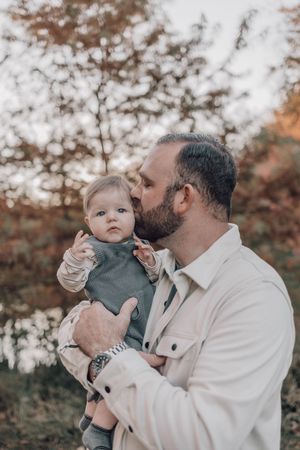 A tender moment between parent and baby in matching white and gray outfits against an autumn backdrop.