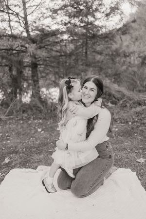Black and white photo of a tender moment between two people sitting on a white blanket outdoors.