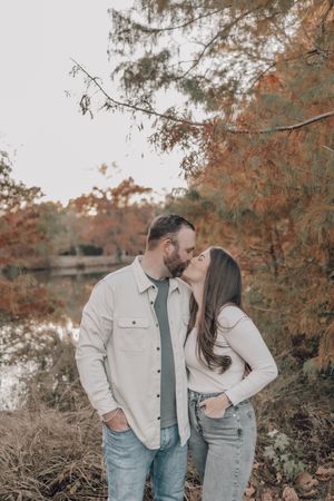 Romantic autumn engagement photos showing a couple embracing under trees with orange and brown fall foliage.