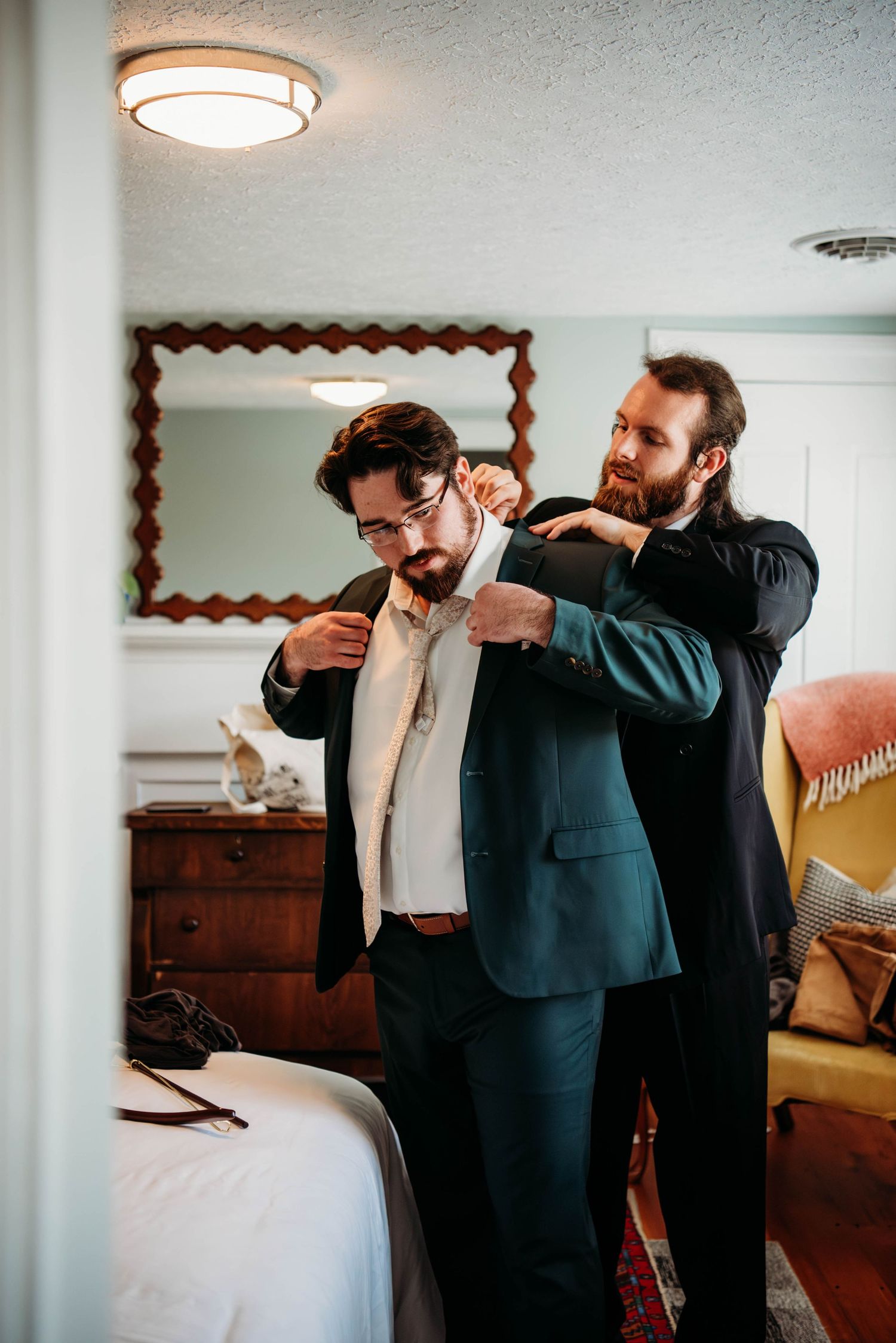 Two people in formal attire help adjust a tie and get dressed before a wedding ceremony.