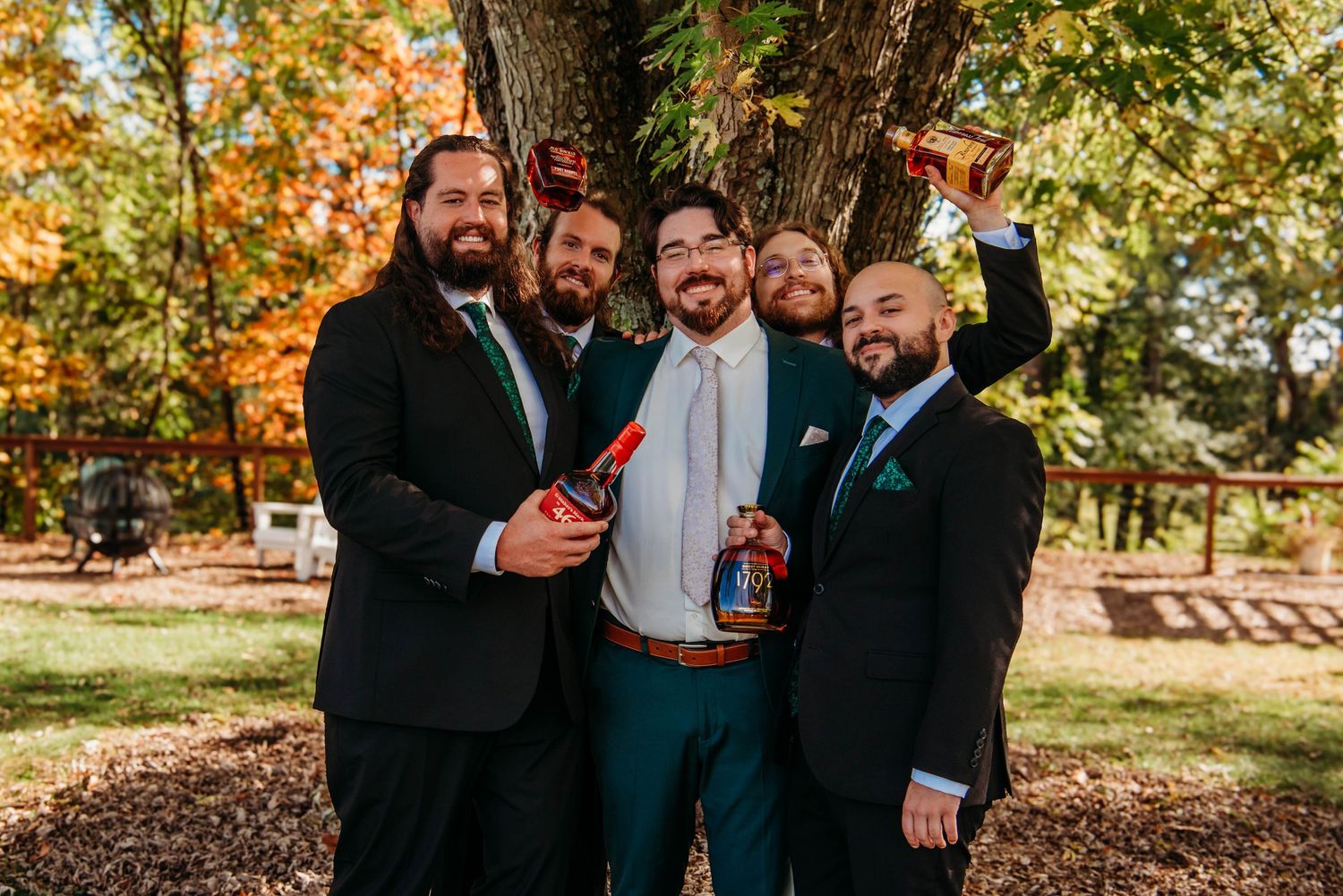 Wedding party members laughing together outdoors with vibrant fall foliage in the background.