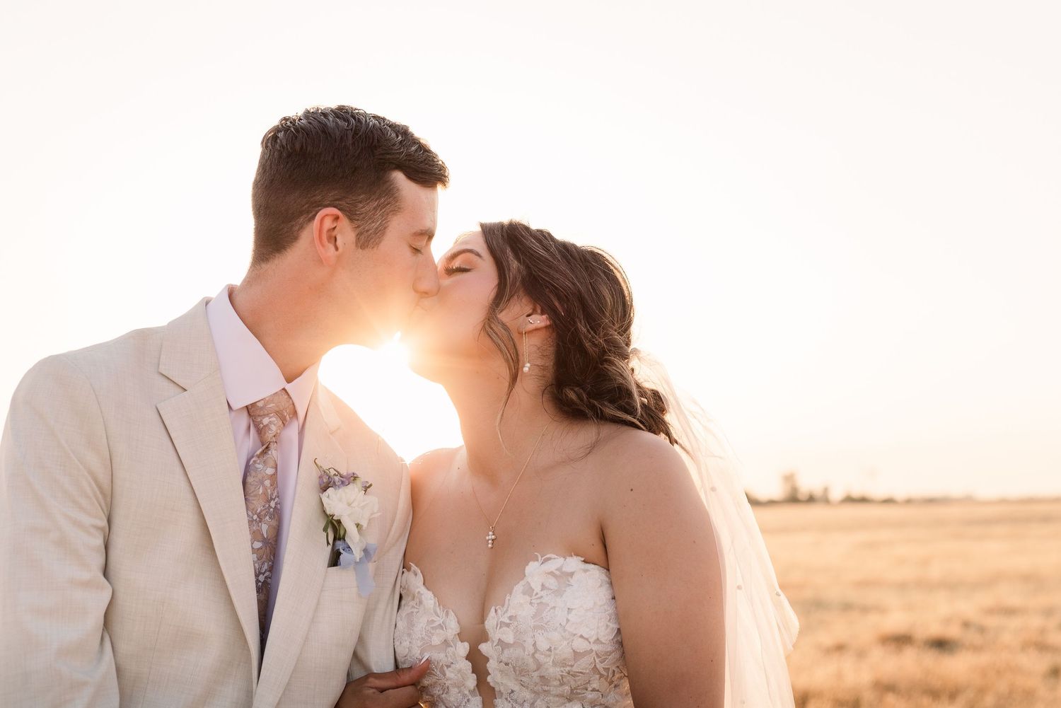 Romantic sunset wedding photos captured in a golden field with mountains in the background.