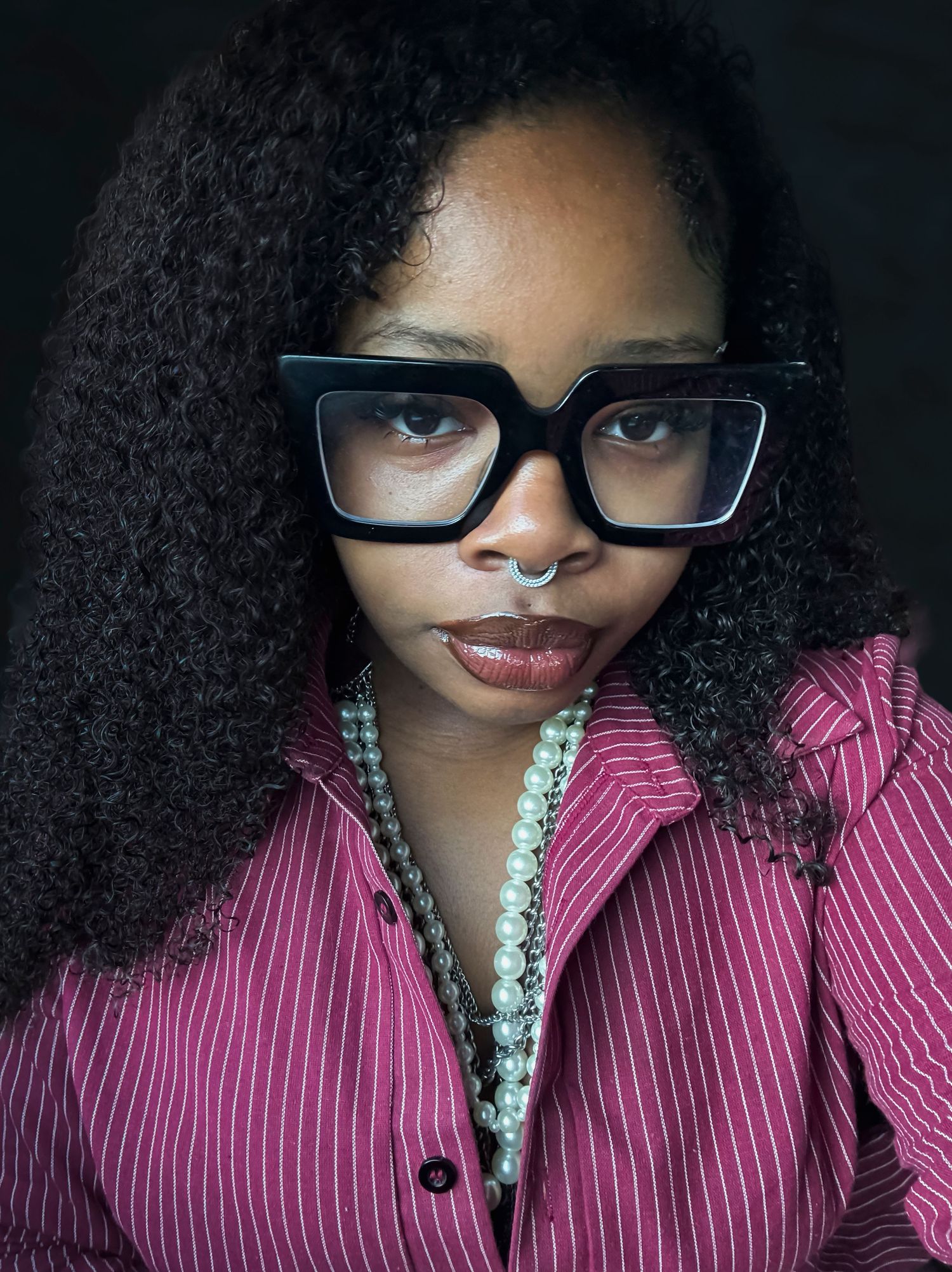 Stylish portrait series featuring curly hair, glasses, and pink striped clothing with pearl necklace.
