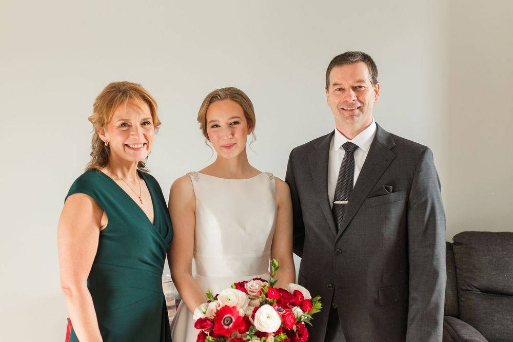 Wedding party members gather in formal attire with red and white bouquets in an elegant indoor setting.