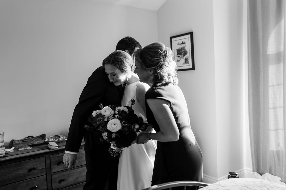 An intimate black and white moment shows people embracing while holding a bouquet of flowers in a sunlit room.