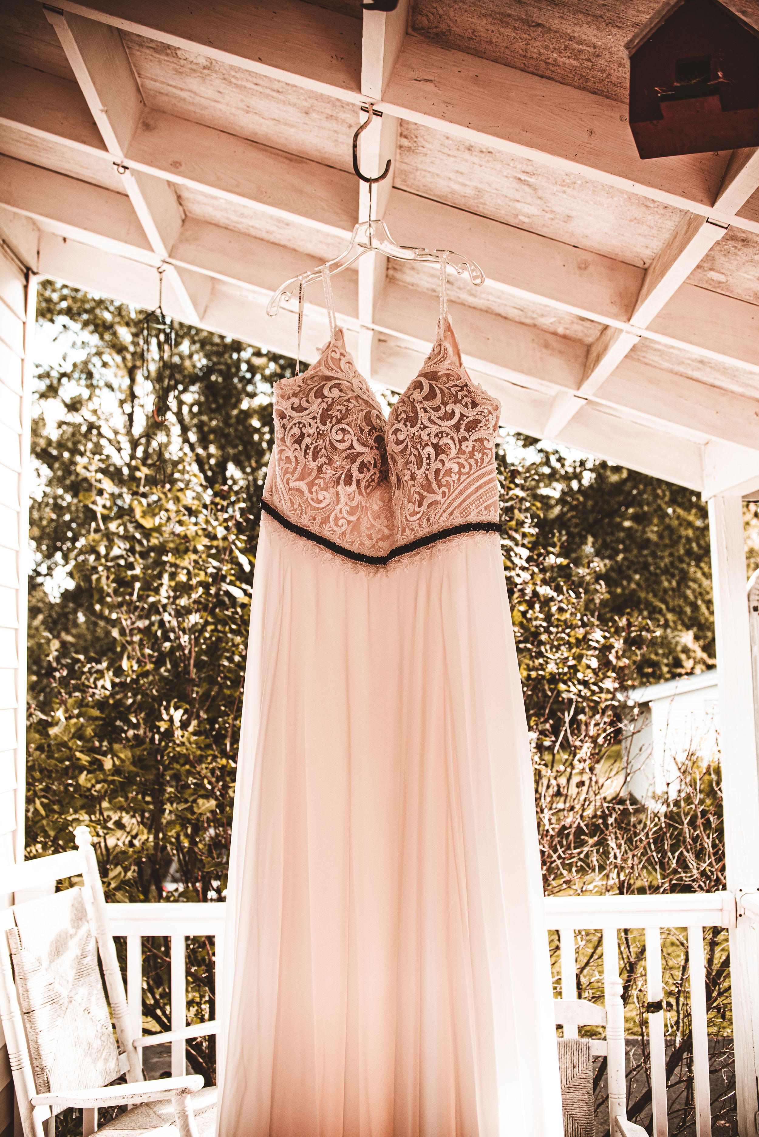 Elegant blush wedding dress with lace bodice hanging from porch ceiling.