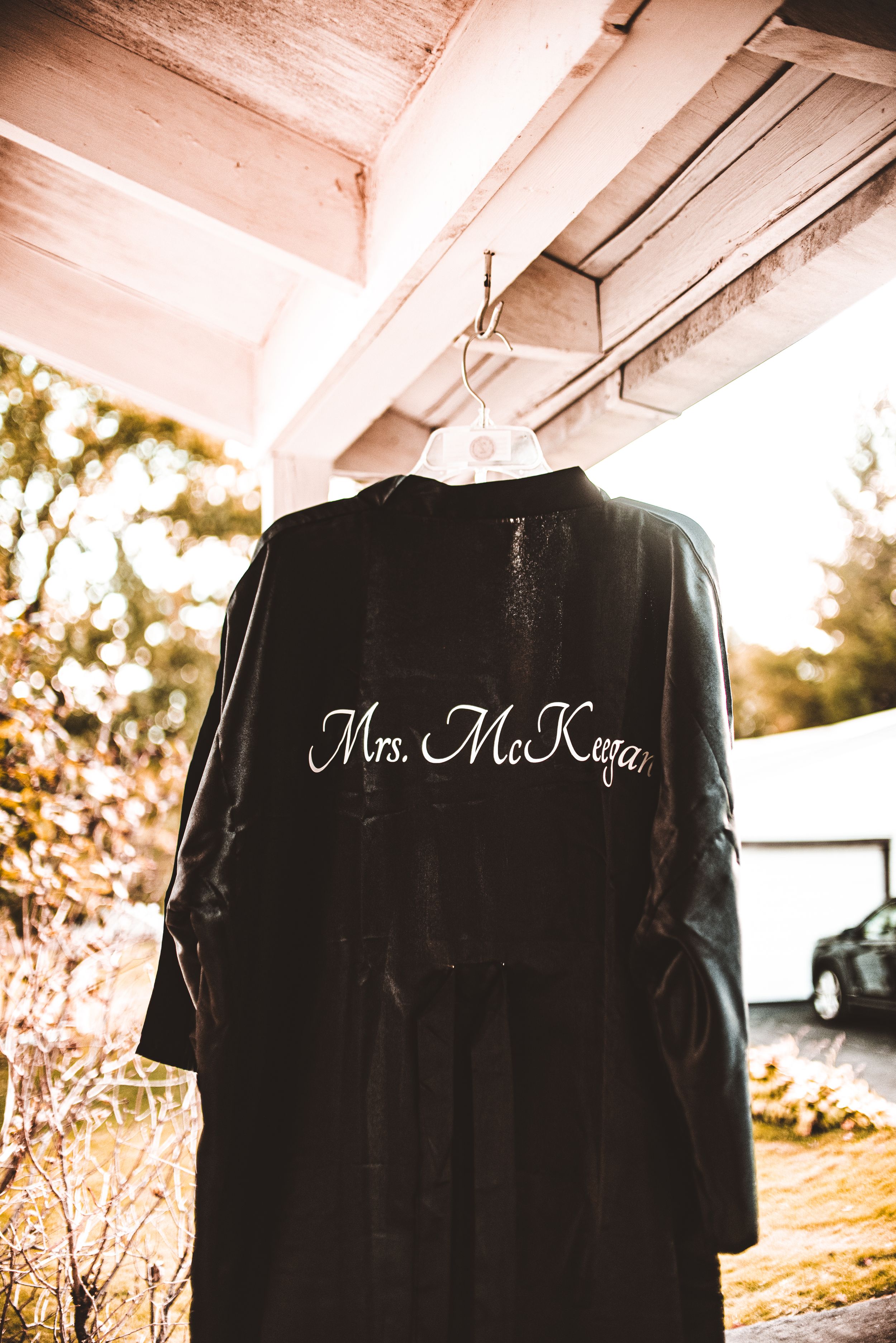 Black bridal robe with 'Mrs. McKeen' embroidered text hanging on porch.