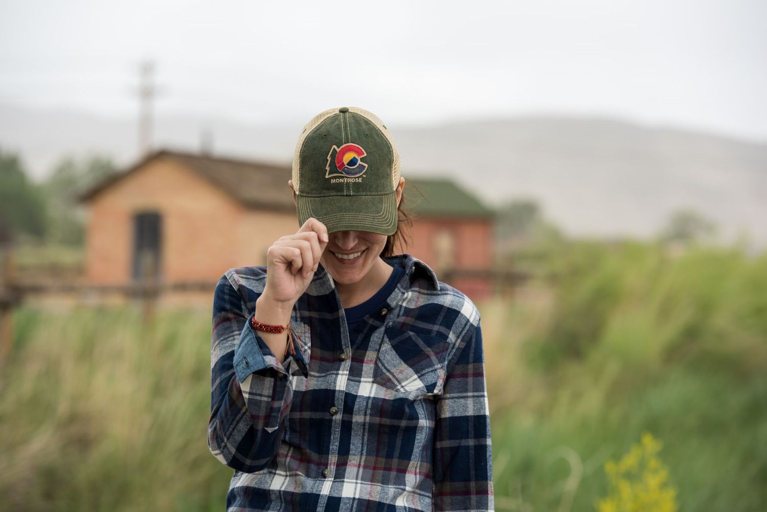 A person in plaid adjusts their cap while standing in a rural field.