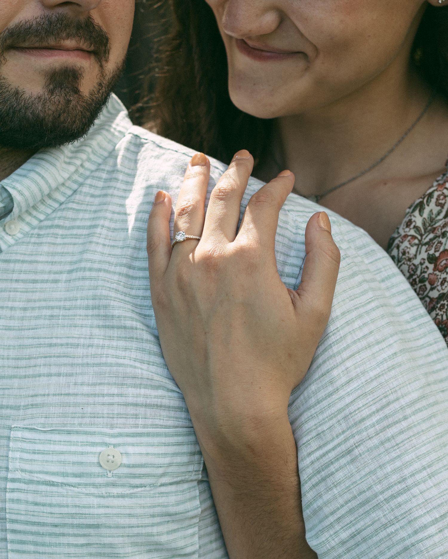 Close-up detail of a hand wearing an engagement ring resting on a striped shirt.