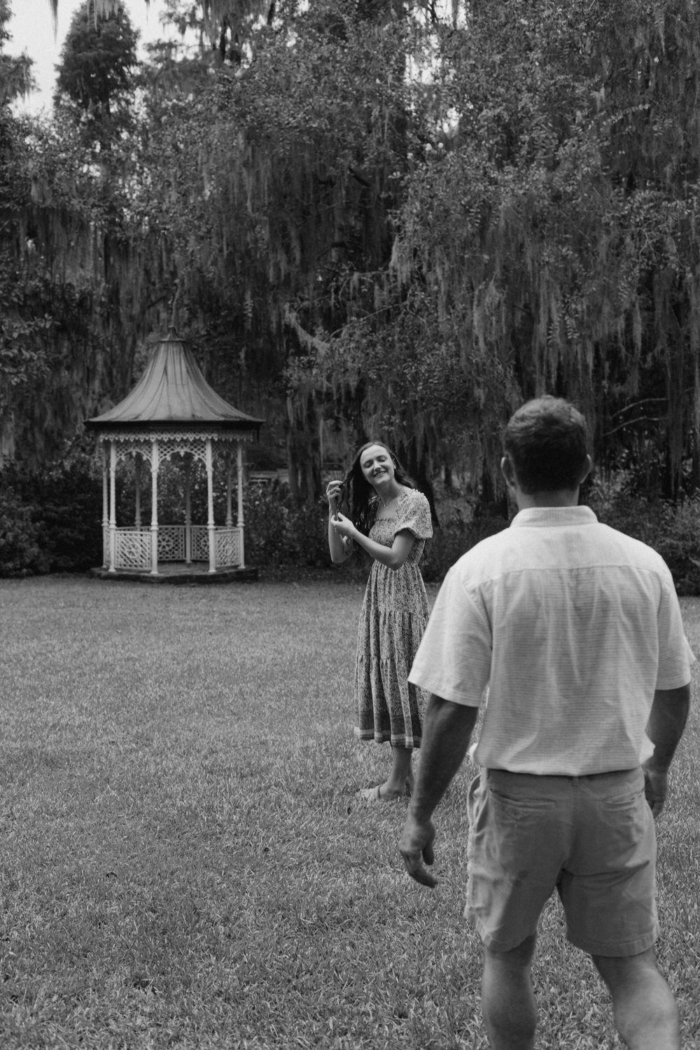 A couple shares a playful moment near a white gazebo in a Southern garden setting.