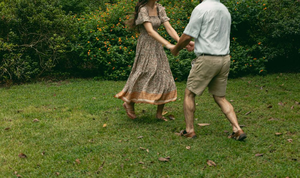 A couple dances together on grass with trees and bushes in the background.