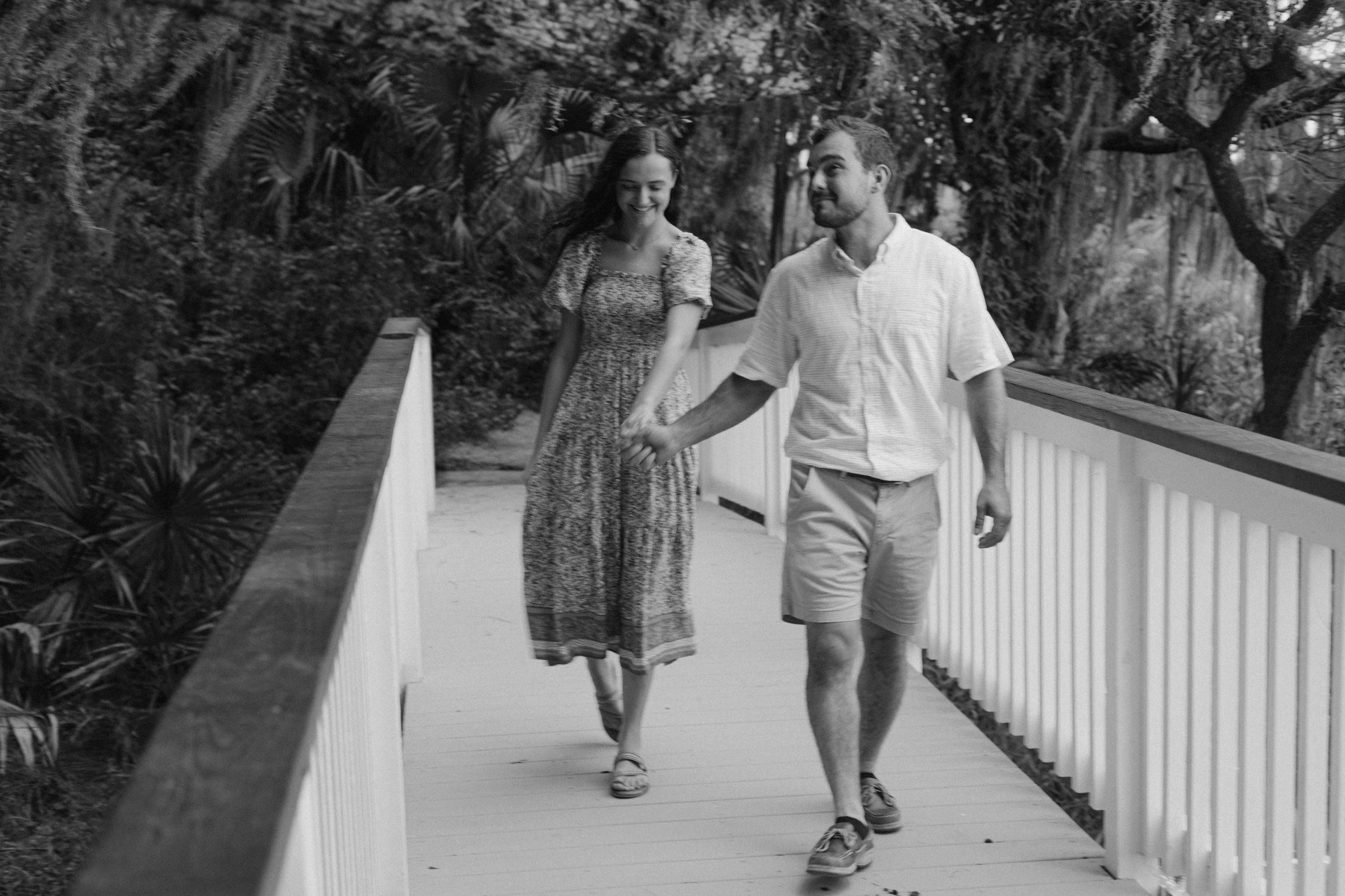 Black and white photo of a couple walking together on a white boardwalk path through nature.