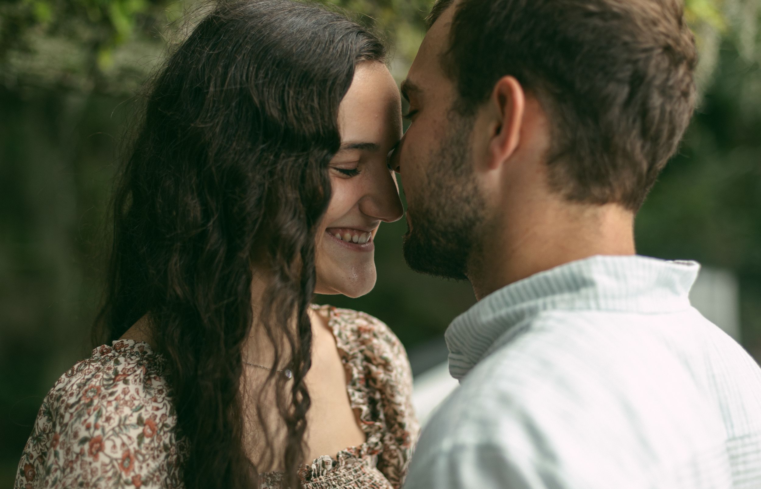 An intimate moment shared between a couple on a walkway with natural greenery in the background.