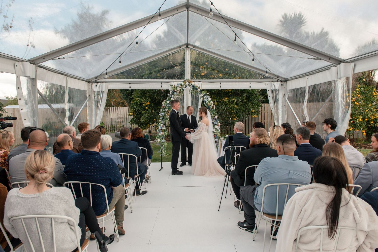 Wedding ceremony in clear tent with white chairs and guests seated on both sides Cambridge New Zealand