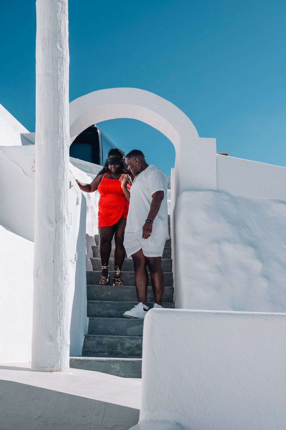 A couple poses on white stairs under an archway in Santorini's signature architecture.