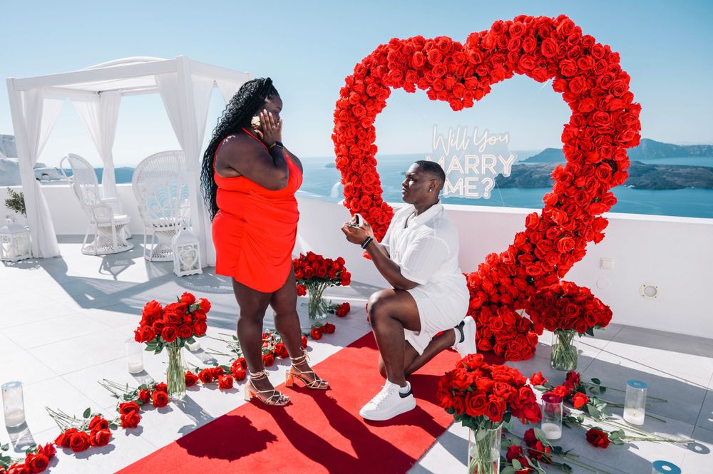 Marriage proposal moment under red rose heart arch on scenic white terrace.