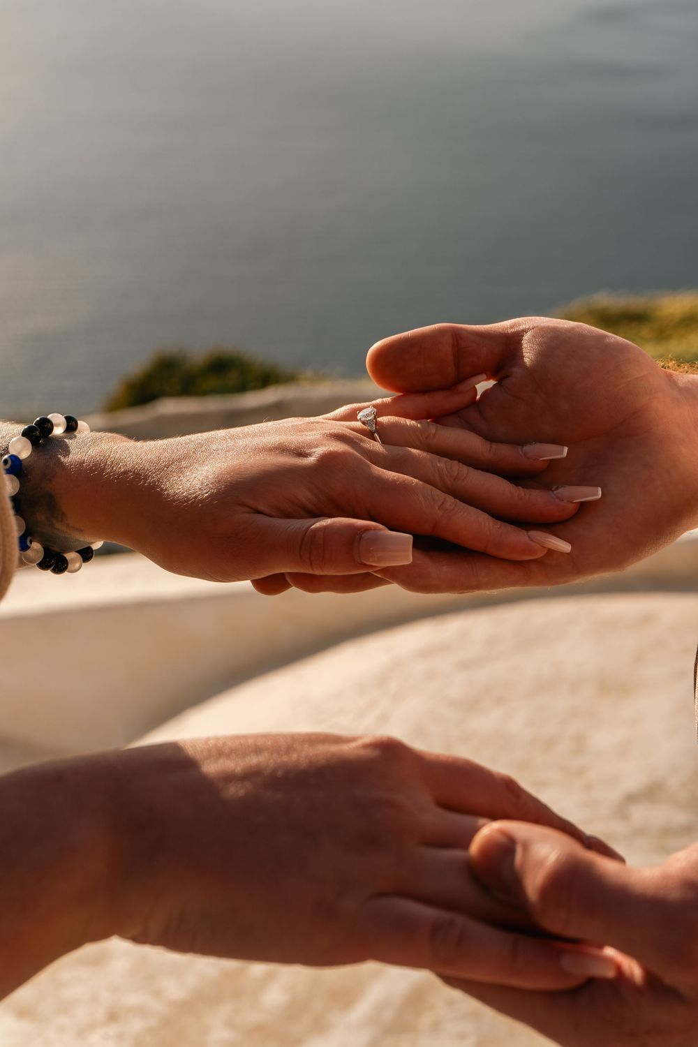 Close-up of a couple exchanging rings by the sea, with a bracelet visible on the woman's wrist.