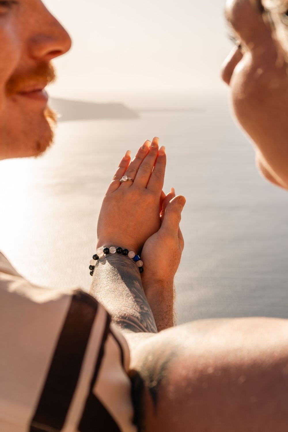 Couple holding hands showing off a diamond engagement ring with ocean views in the golden sunset light.