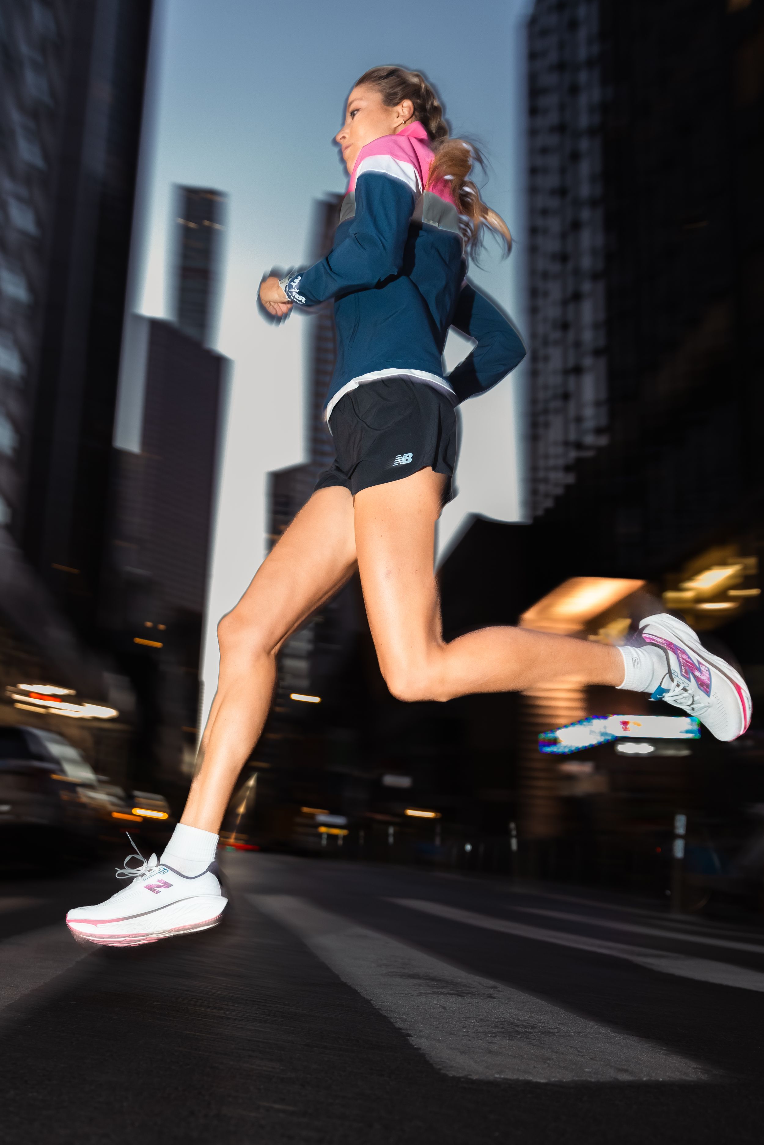 Athletic figure running through city streets at dusk wearing navy and pink activewear.