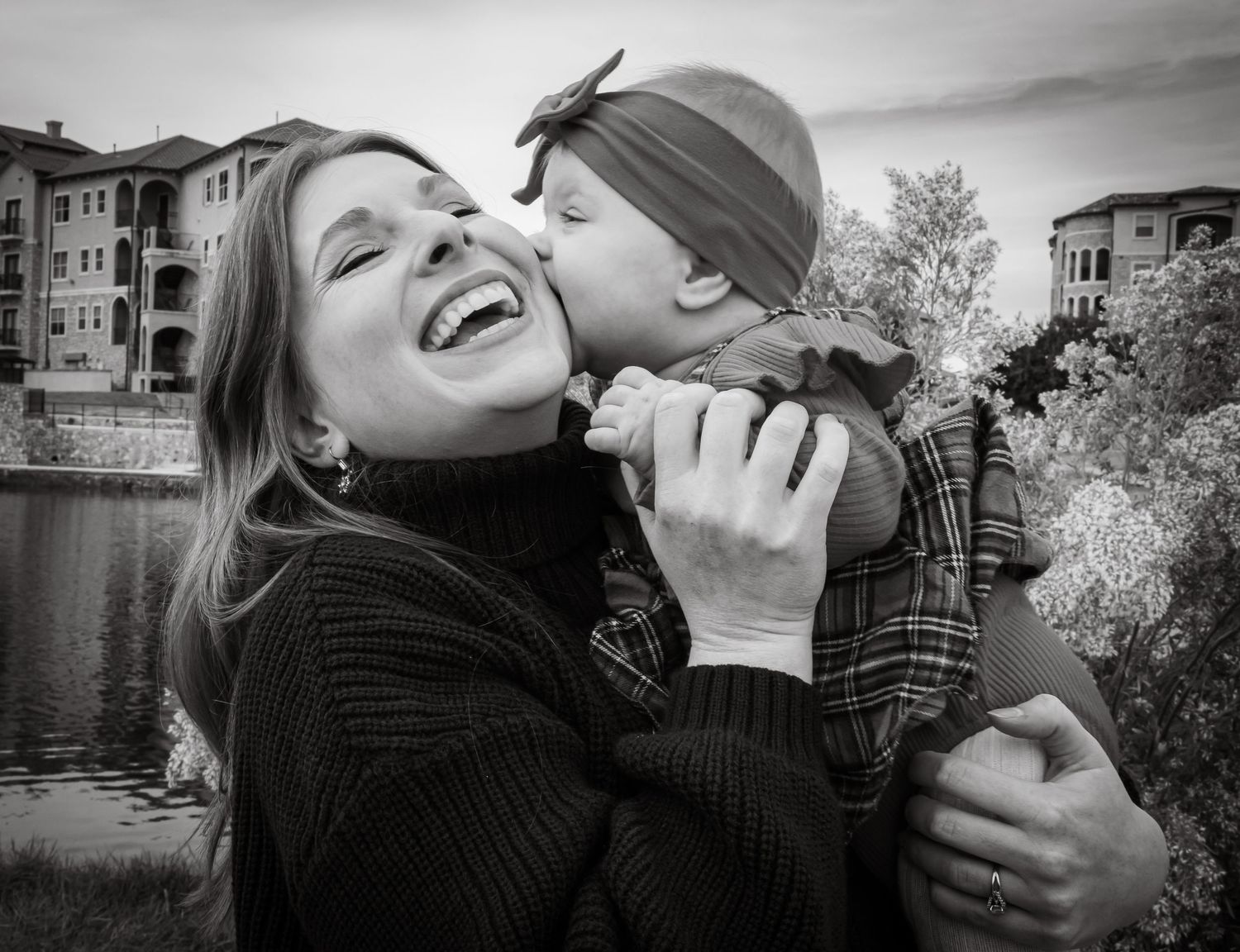 Black and white photo of a laughing mother receiving a sweet kiss from her young child.