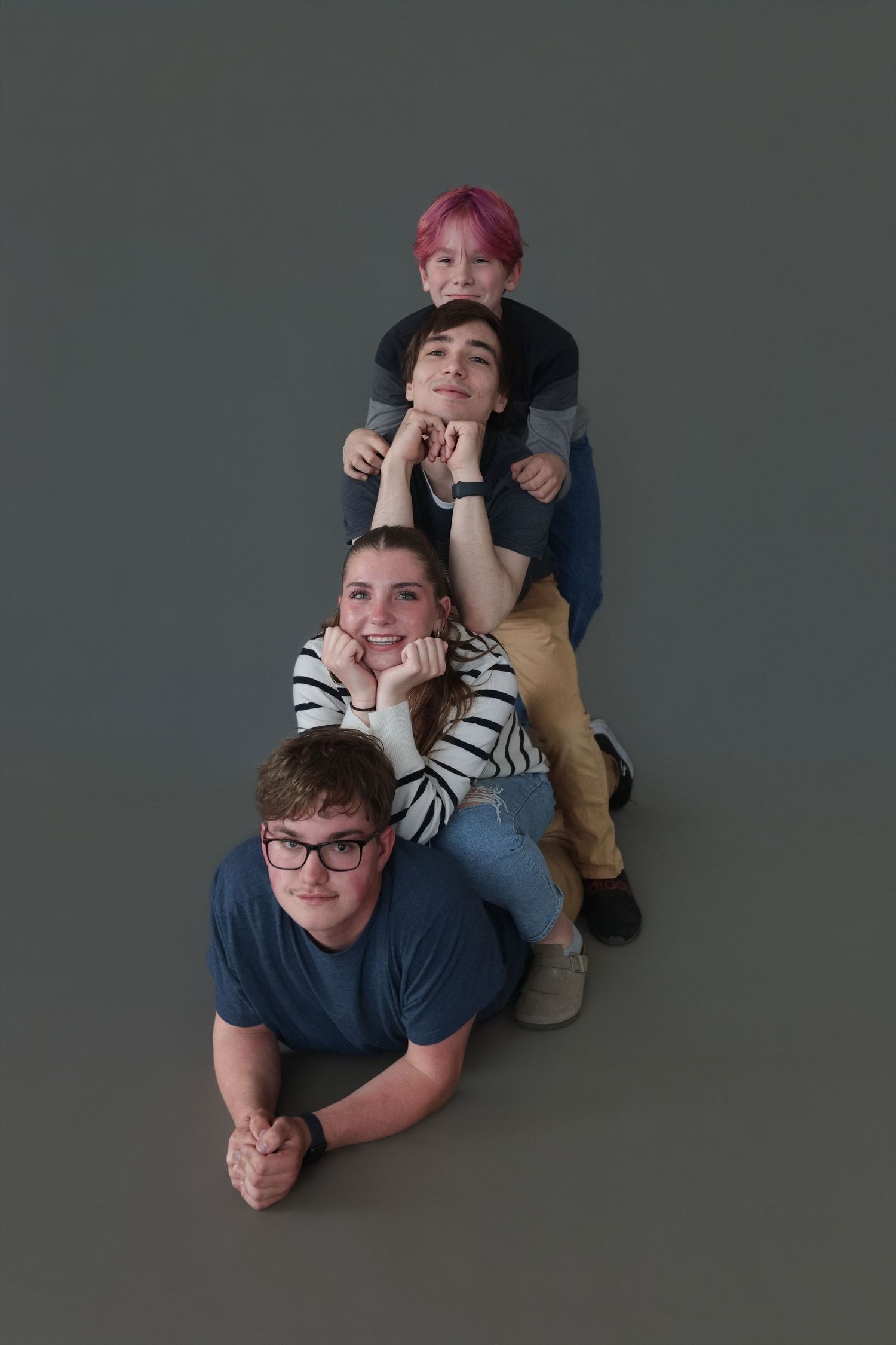Four people stacked on top of each other lying on the floor in a creative portrait pose against a gray background.