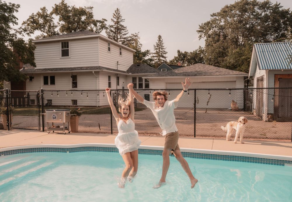 Two people jumping into a swimming pool together on a summer day.