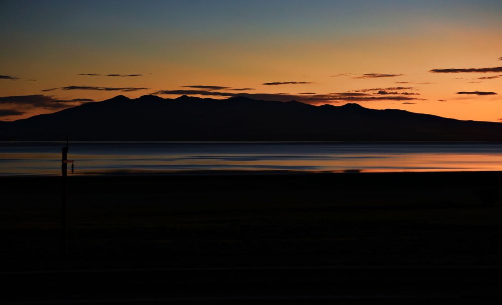 A dramatic sunset silhouettes mountain ranges against a darkening sky with orange and purple hues on the horizon.