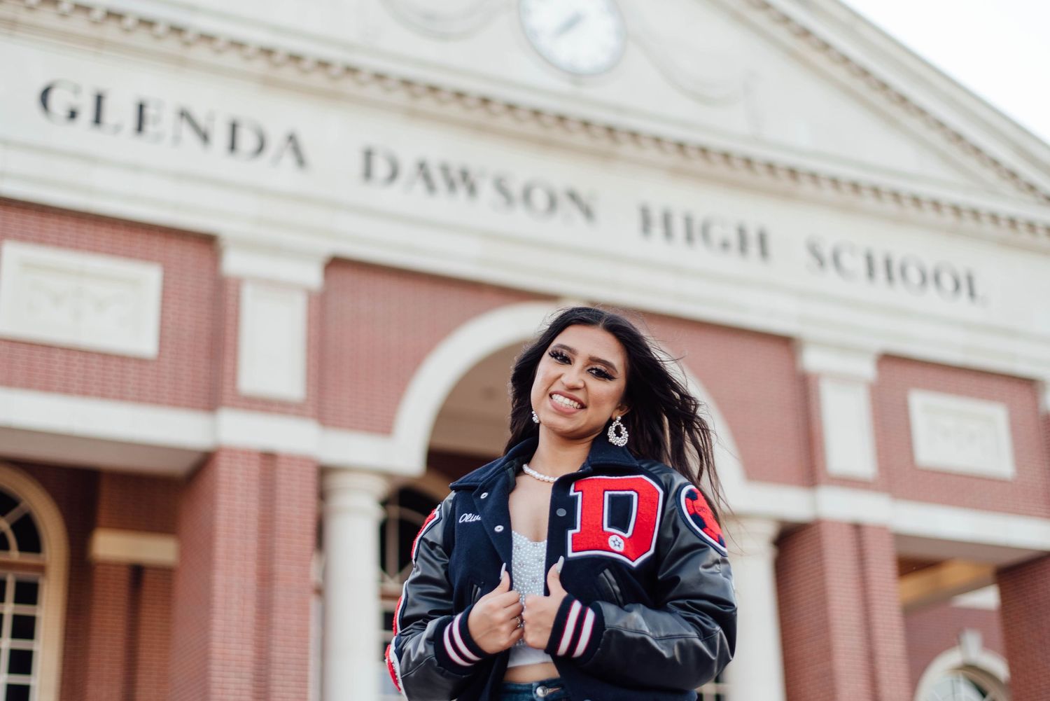 A Houston high school senior confidently posing in front of her school, celebrating her achievements and graduation