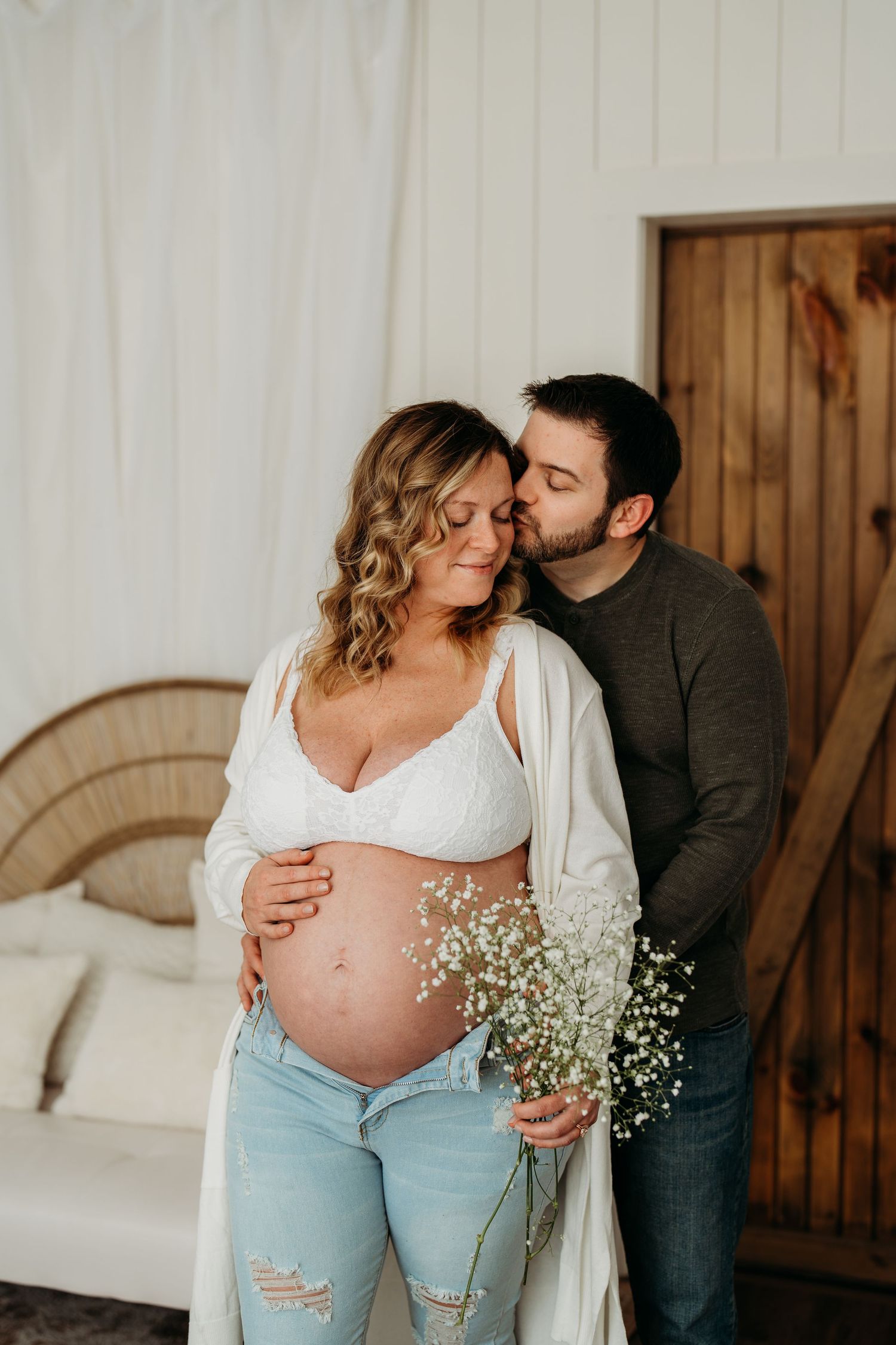 Intimate maternity photo with baby's breath flowers against wooden door backdrop.