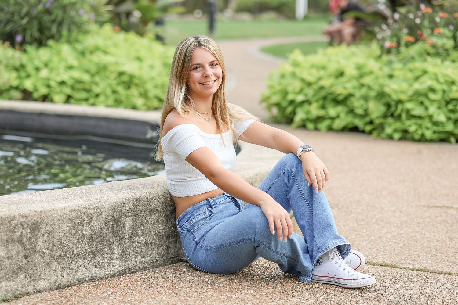 A casual portrait of someone in jeans and white top sitting by a garden water feature.