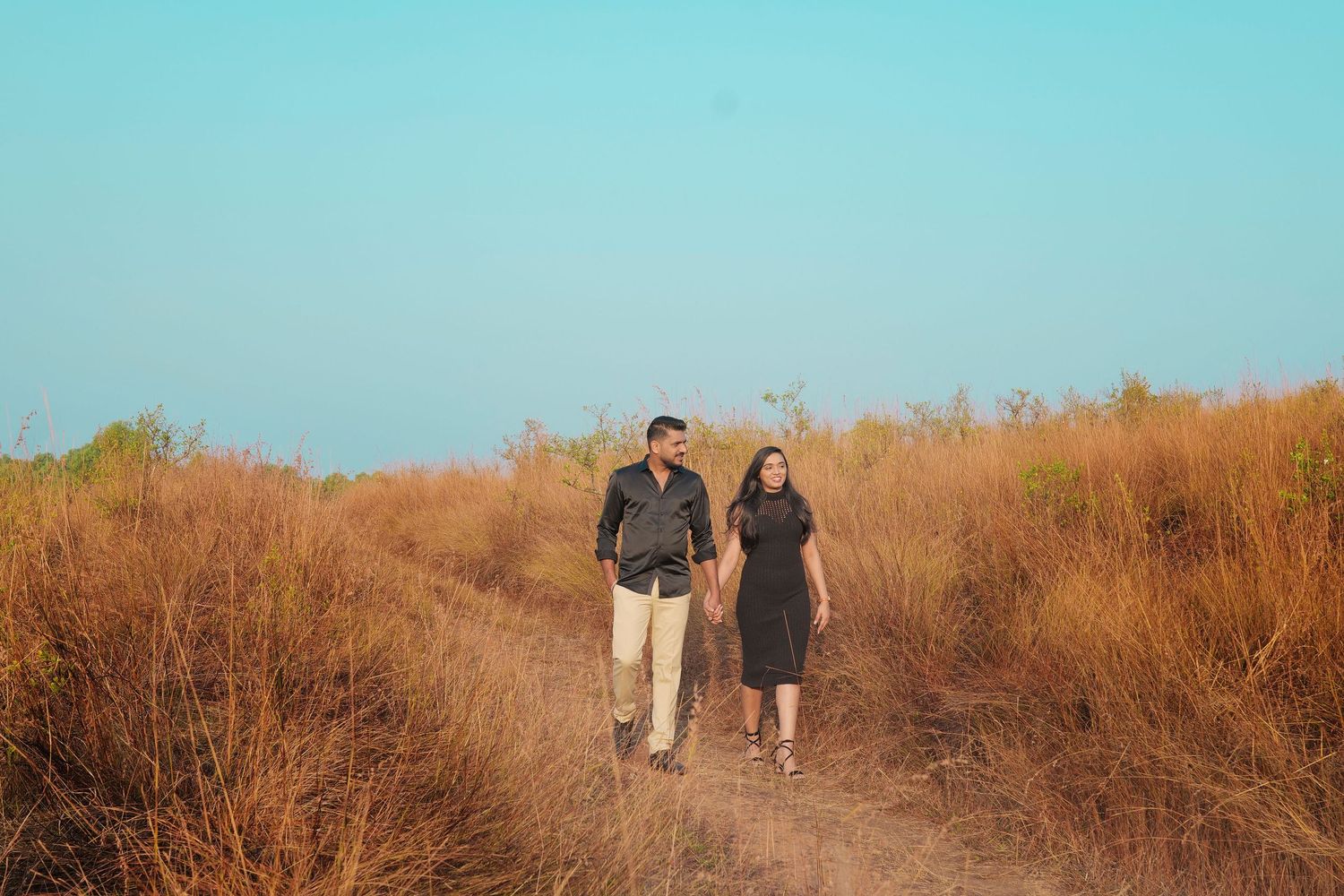 Couple walking together through a field during an outdoor pre-wedding photoshoot
