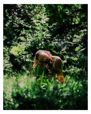Person with red hair resting among lush green foliage and grass in natural outdoor setting.