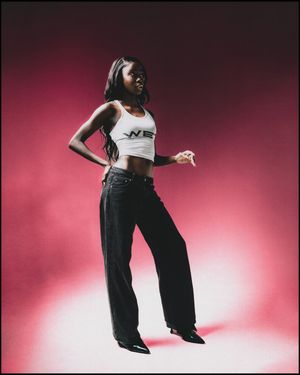 A slim Black woman in a white WET crop top and black wide-leg pants poses against a pink gradient background.