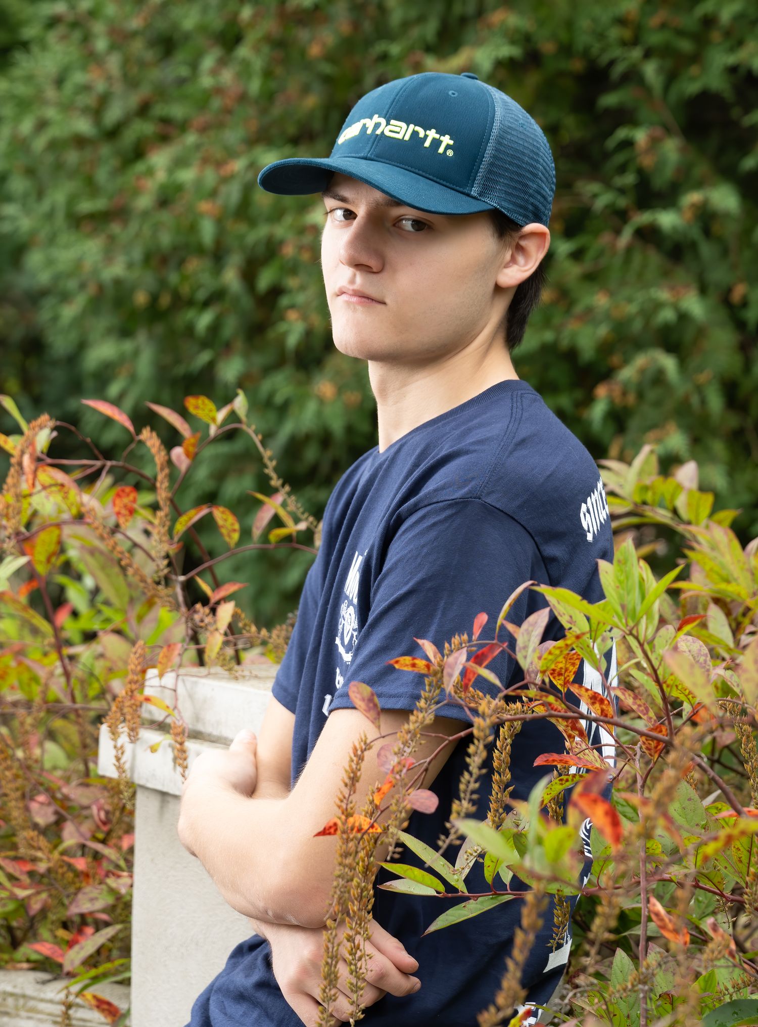 Casual portrait of person in blue cap and navy shirt against autumn foliage.