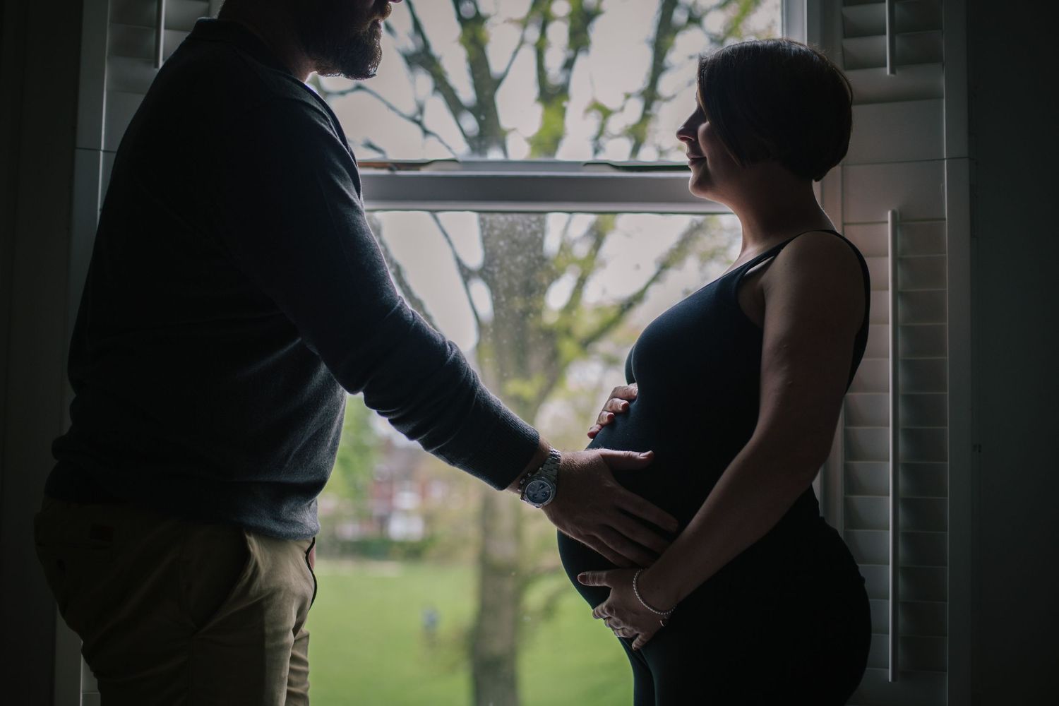 A tender silhouette of an expectant couple by a window with natural light.