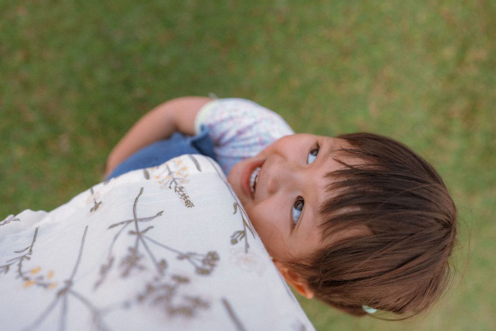 Close-up portrait of child lying on grass looking up with curious expression.